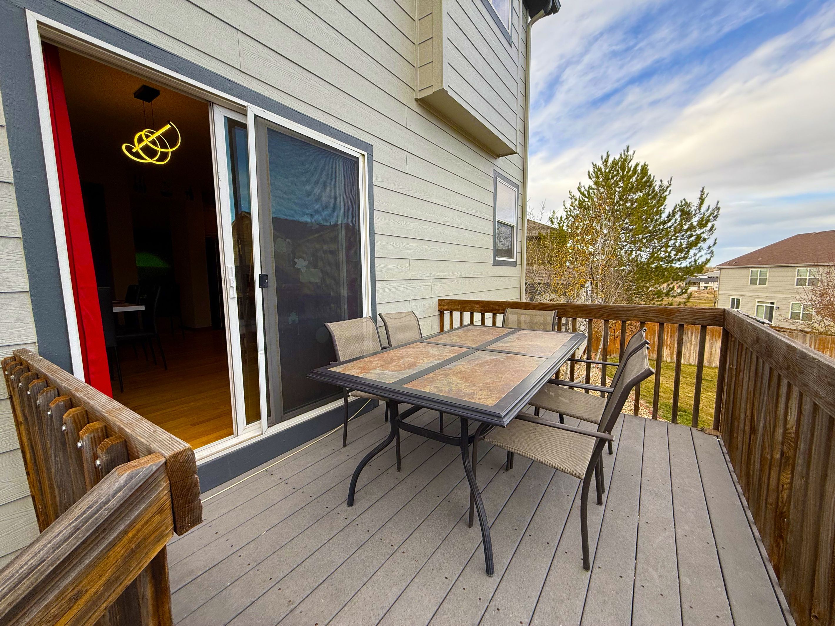 Une terrasse avec une table et des chaises, une porte-fenêtre coulissante et une vue sur la maison voisine.