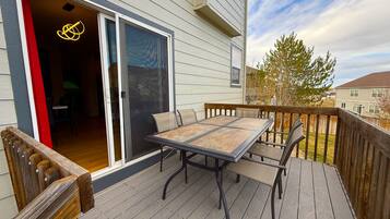 Une terrasse avec une table et des chaises, une porte-fenêtre coulissante et une vue sur la maison voisine.