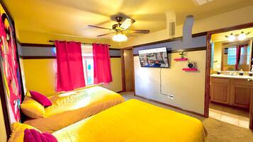 Habitación con dos camas, ventilador de techo, televisión montada en la pared y baño con espejo y lavamanos.
