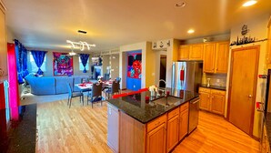 A modern kitchen with wooden cabinets, a stainless steel refrigerator, and a dining area with a blue sofa and a table set for two. - GolfSim HotTub PS5 Sauna Thtr Pooltbl 6BR 5BA 420 (Thornton, CO, 80602)