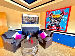 A living room with two grey armchairs, a round coffee table with a vase and a red sculpture, a fireplace, and a large colorful painting on the wall. - GolfSim HotTub PS5 Sauna Thtr Pooltbl 6BR 5BA 420 (Thornton, CO, 80602)