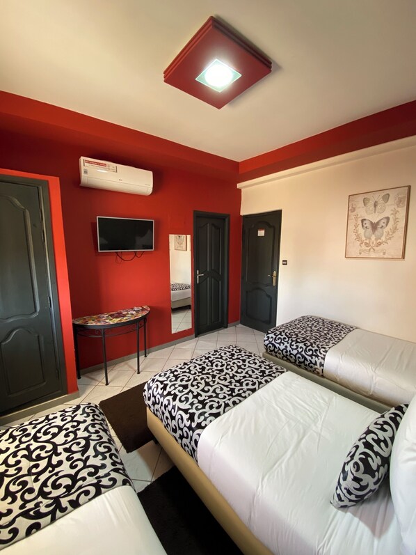 A hotel room with two beds, a TV, an air conditioning unit, and a small table. - VELSATIS (Beni Mellal)
