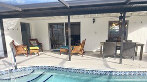 Un espace piscine extérieur abrité, doté de chaises longues et d’une table, entouré de murs blancs et bordé d’une piscine carrelée.