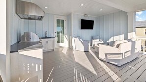 A spacious outdoor living area with a modern kitchen, comfortable seating, and a flat-screen TV mounted on the wall.