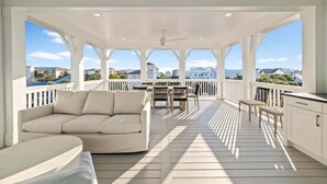 A covered outdoor area with a sofa, dining table, and chairs, overlooking a scenic view.