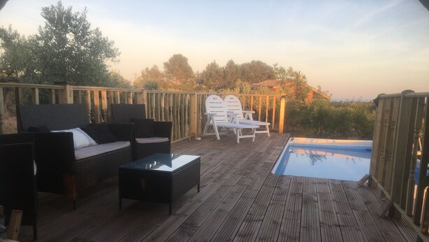 A wooden deck with outdoor furniture, a pool, and a view of trees and buildings. - Lovely 4-bed Villa in L'ametlla de Mar, off Grid , (L'Ametlla de Mar)