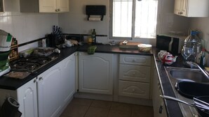 A kitchen with white cabinets, a gas stove, a window with blinds, and various kitchen items on the counter. - Lovely 4-bed Villa in L'ametlla de Mar, off Grid , (L'Ametlla de Mar)