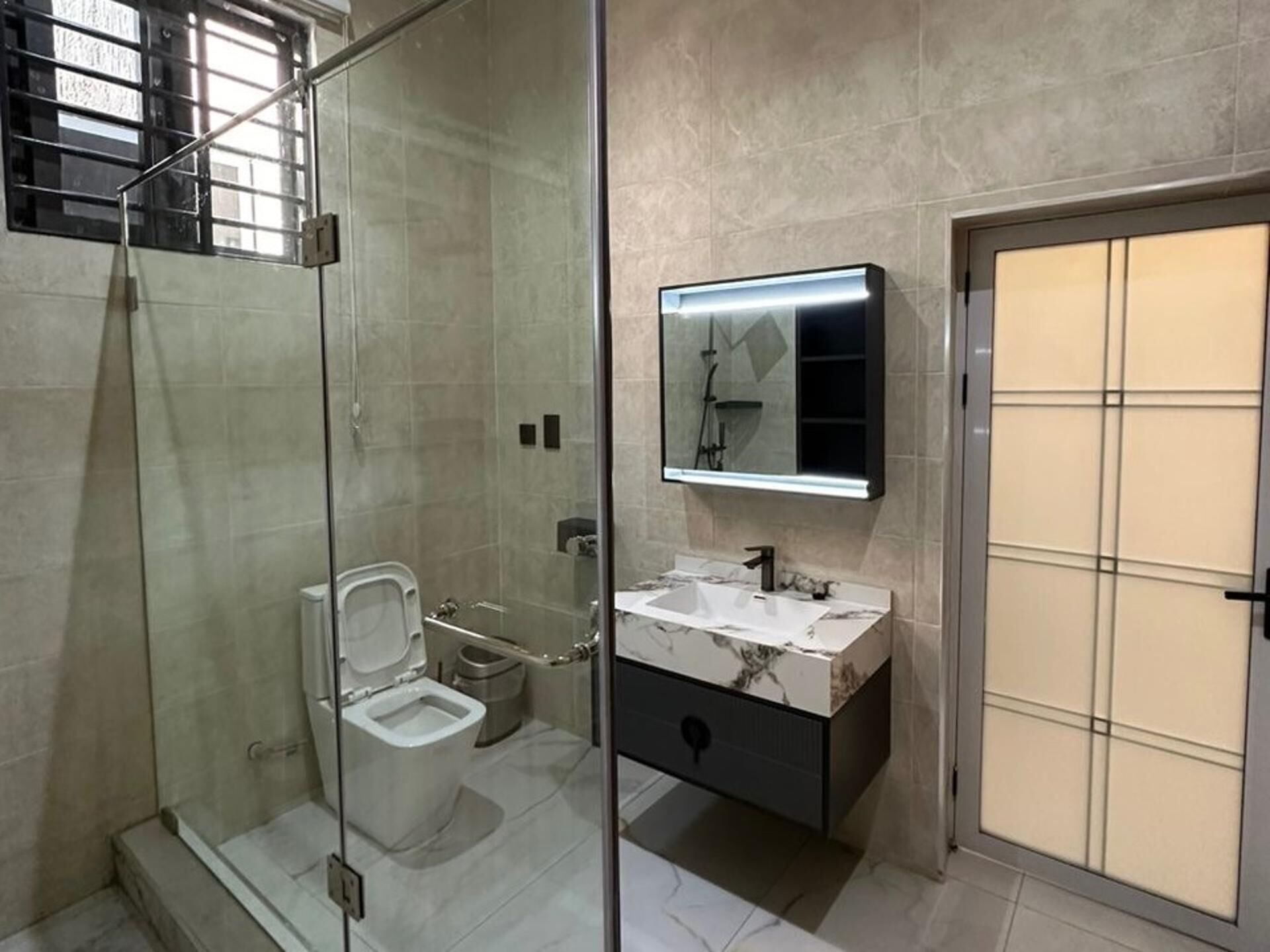 Un baño moderno con cabina de ducha de vidrio, inodoro, lavabo con espejo y un armario.