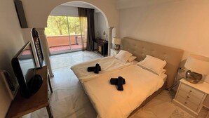 Une chambre d’hôtel avec un grand lit, un bureau avec un ordinateur, une chaise et une vue sur un balcon doté d’une balustrade.