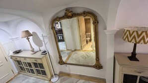 Une salle de bain dotée d’un grand miroir décoratif, d’une coiffeuse avec miroir et de toilettes visibles à travers une arche.