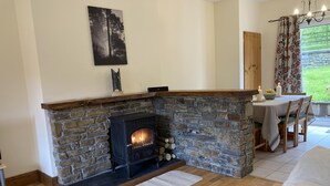 Un accogliente soggiorno con camino in pietra, pavimento in legno, zona pranzo con tavolo e sedie e un quadro appeso al muro.