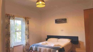 Una camera da letto con un letto, una finestra con tende, un quadro appeso al muro e un lampadario al soffitto.