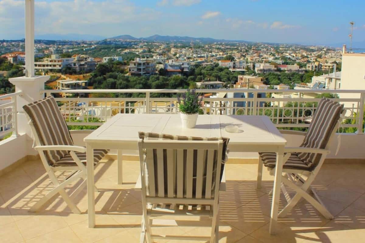 A terrace with a table and chairs, a potted plant, and a view of a town.