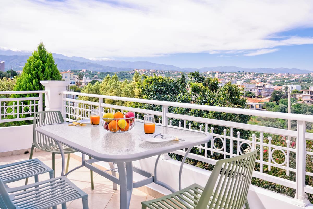 A balcony with a table set for two, a fruit bowl, and a glass of orange juice.