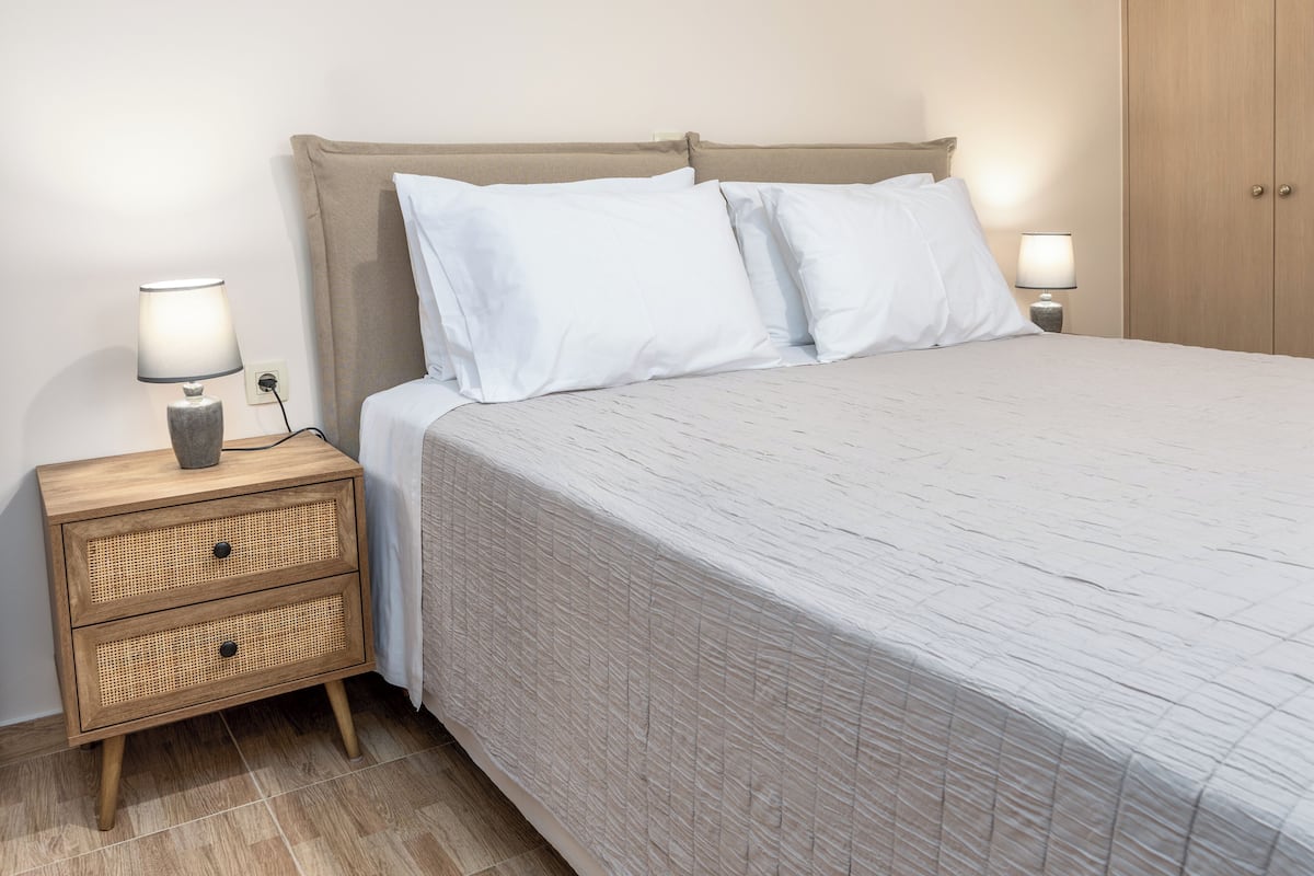 A neatly made bed with white linens, a wooden nightstand with a lamp, and a wooden wardrobe.