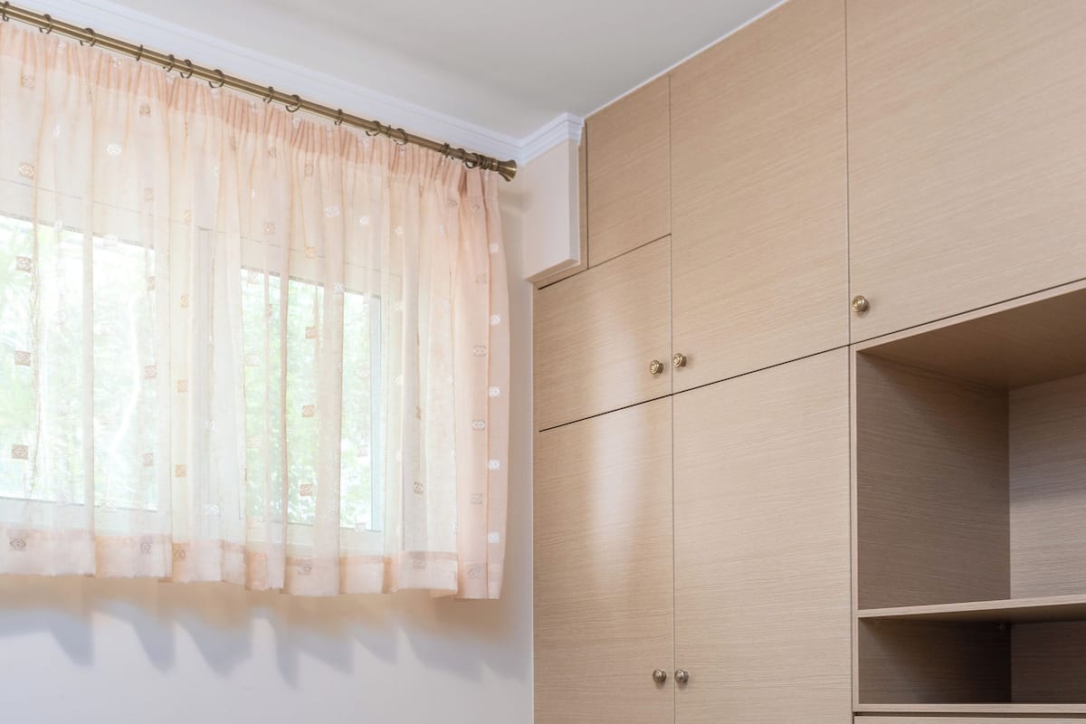 A bedroom with a bed, a wardrobe, and a window with sheer curtains.