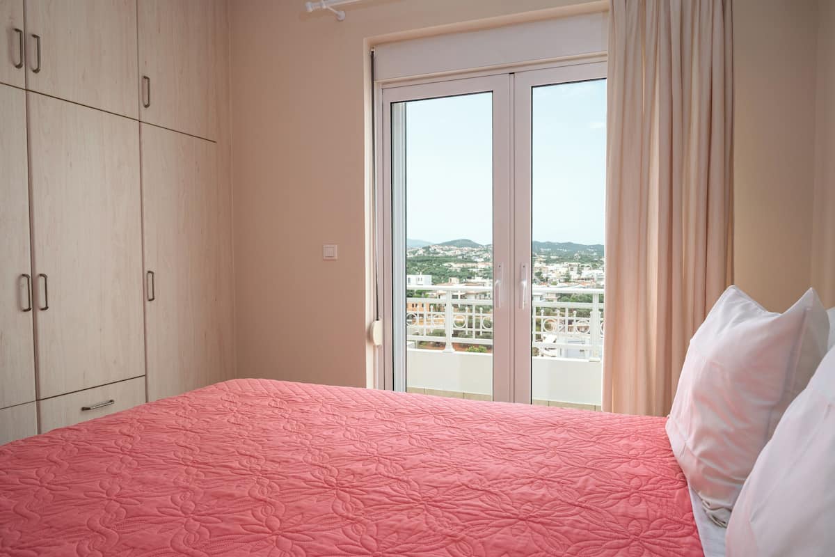 A bedroom with a bed, a window with curtains, and a view of buildings.
