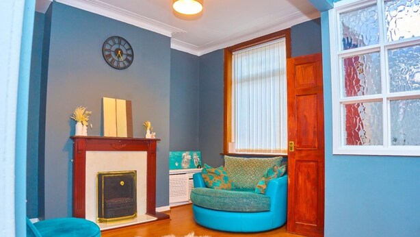 A living room with a fireplace, a clock, a window with blinds, and a blue sofa.