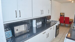 A modern kitchen with white cabinets, a black countertop, a blue toaster, a microwave, a gas stove, and a red dining chair.
