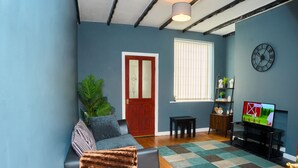 A living room with a sofa, a coffee table, a TV, a clock, and a window with blinds.