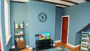 A living room with a television displaying a children's show, a black entertainment unit, a wooden cabinet, a clock, and a staircase.