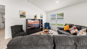 A modern living room with a grey sofa set, a flat-screen TV, and a dining area with a table and chairs.