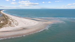 An aerial view of a beach with a wide sandy shore, a clear blue sky, and a calm sea. - BHI Club + On Course + Sleeps 10 + 2 Carts (Bald Head Island)