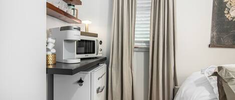 Un dormitorio compacto con cama, una kitchenette pequeña con microondas y un ventanal con cortinas.