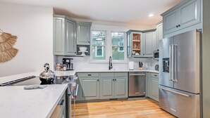 A modern kitchen with light green cabinets, stainless steel appliances, and a white marble countertop. - BHI Club + On Course + Sleeps 10 + 2 Carts (Bald Head Island)
