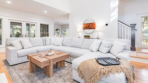 A modern living room with a large sectional sofa, a wooden coffee table, and a round wall clock. - BHI Club + On Course + Sleeps 10 + 2 Carts (Bald Head Island)