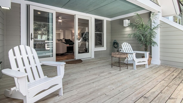 A covered porch with two Adirondack chairs, a wicker table, and a potted plant. - BHI Club + On Course + Sleeps 10 + 2 Carts (Bald Head Island)