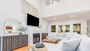 A modern living room with a grey sofa, a wooden coffee table, a fireplace, and a large mirror. - BHI Club + On Course + Sleeps 10 + 2 Carts (Bald Head Island)