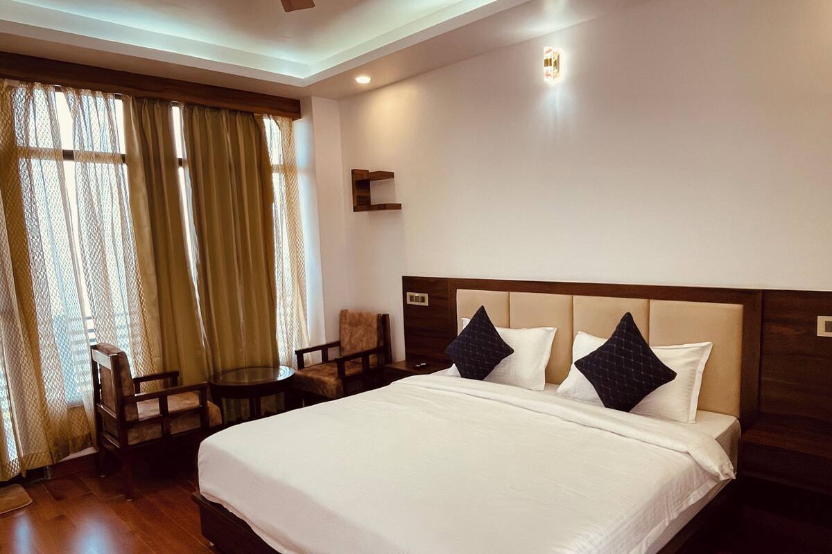 Une chambre d’hôtel avec un grand lit, deux chaises, une petite table et une fenêtre avec des rideaux.