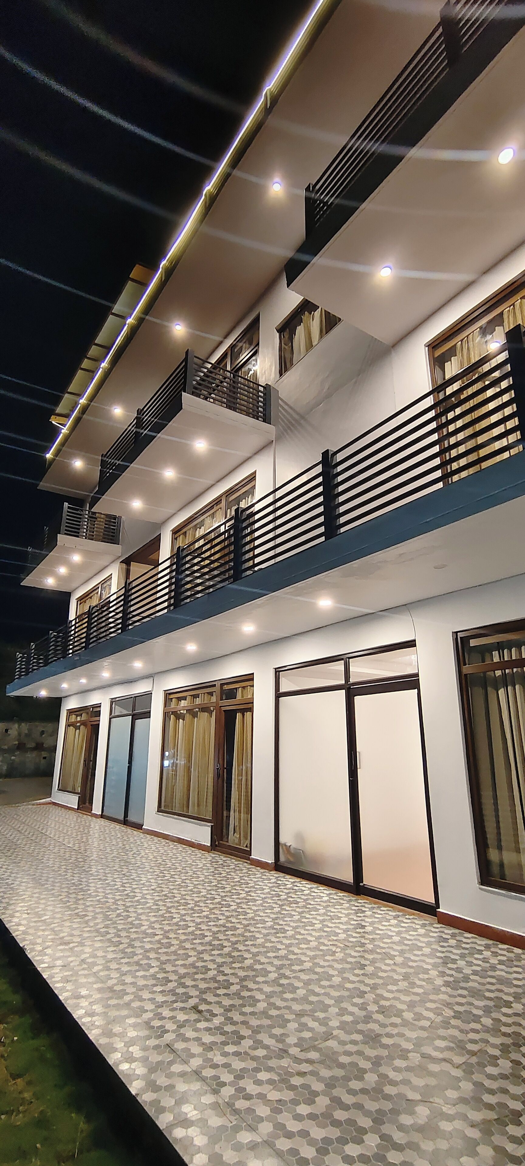 A multi-story building with balconies, large windows, and a patterned walkway.
