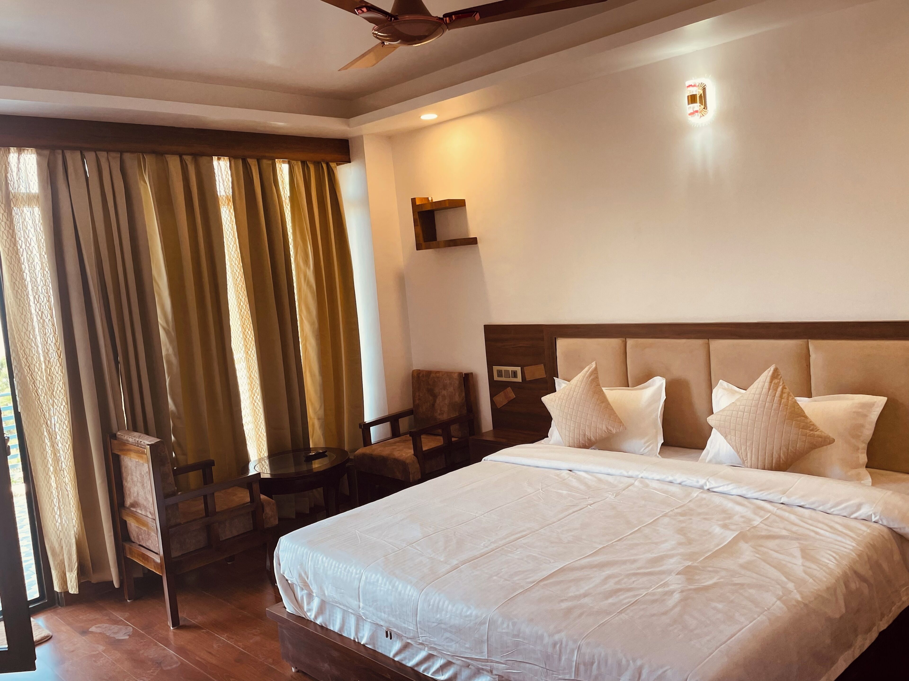 Quarto de hotel com uma cama grande, cabeceira de madeira, escrivaninha com cadeira e janela com cortinas.