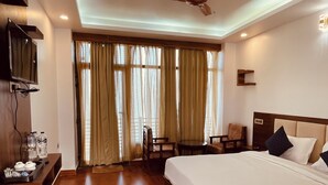 Ein Hotelzimmer mit einem großen Bett, einem Schreibtisch mit Stuhl, einem an der Wand befestigten Fernseher und einem Fenster mit Vorhängen.