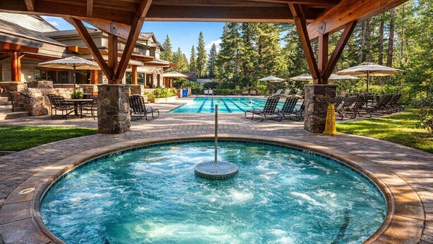 A hot tub surrounded by stone tiles, with lounge chairs and umbrellas in the background.