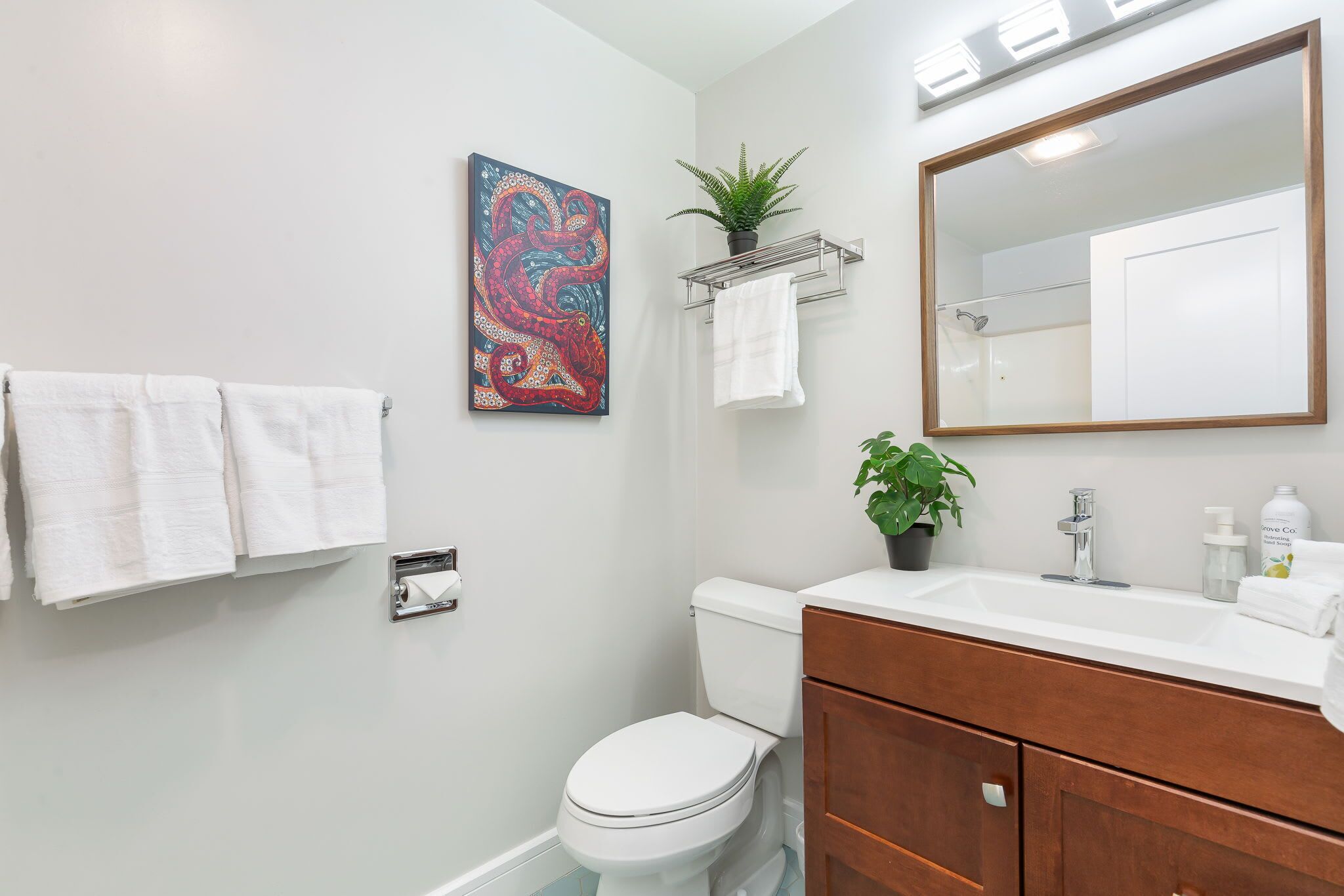Un baño con un inodoro blanco, un tocador de madera con un lavabo, un espejo y una obra de arte colorida en la pared.