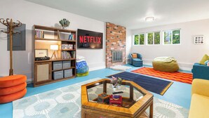 A living room with a bookshelf, a Netflix sign, a brick wall, a blue carpet, and a yellow armchair. - Renovated Home | Dogs OK | Large Deck (Seattle)