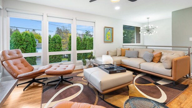 A modern living room with a leather chair, a sofa, and a coffee table. There are large windows with a view of trees and a balcony. - Renovated Home | Dogs OK | Large Deck (Seattle)