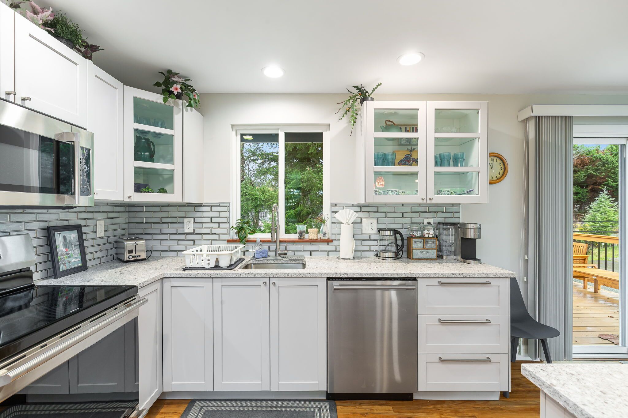 A modern kitchen with white cabinets, a stainless steel dishwasher, and a large window providing a view of the outdoors.