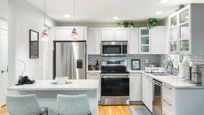 A modern kitchen with white cabinets, stainless steel appliances, and a central island with bar stools. - Renovated Home | Dogs OK | Large Deck (Seattle)
