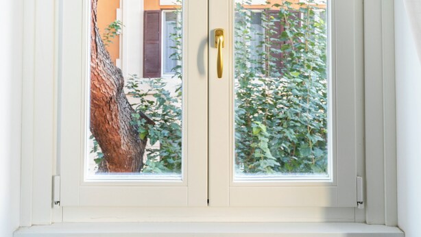 A window with a view of a building with multiple balconies and a tree in the foreground. - Charming Home near San Giovanni (Rome)