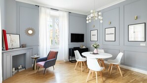 A modern living room with a fireplace, a dining area with white chairs, a TV mounted on the wall, and framed artwork. - Charming Home near San Giovanni (Rome)