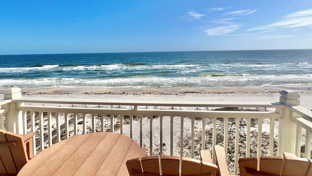 Une terrasse en bois avec une table et des chaises, donnant sur une plage où l’on peut admirer les vagues.
