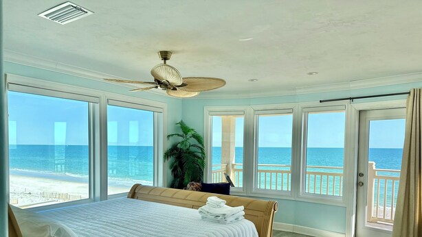A bedroom with a large bed, a ceiling fan, and a view of the ocean through multiple windows. - Moonlight Sonata - Gulf Front (St. George Island)