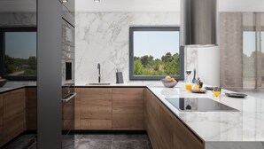 A modern kitchen with a large window, marble countertops, wooden cabinets, and a built-in oven. - Penthouse Adela (Vir)
