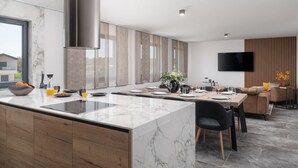 A modern kitchen with a marble island, wooden cabinets, and a dining area with a sofa and TV. - Penthouse Adela (Vir)
