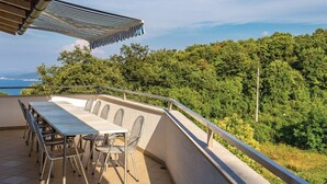 An outdoor terrace with a dining table and chairs, overlooking a lush green landscape and the sea.