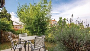 An outdoor patio with a table and chairs, surrounded by greenery and a stone wall.